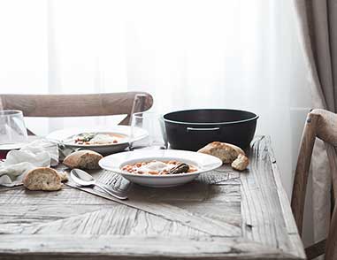 Накрытый стол, на переднем плане тарелка с супом, хлеб и ложка